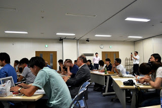 席に着いたたくさんの参加者がメモを取ったり前を向いて話に聞き入ったりしている様子の写真