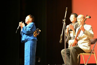 舞台の上で三味線の演奏にあわせて和服姿の人々が唄や手拍子を披露している伝統芸能の写真