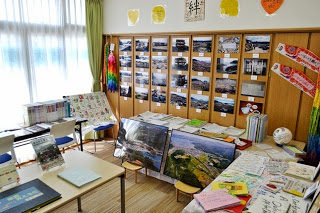 窓から柔らかい光が差し込む明るい学習室で、壁には被災地の写真が掲示されていて、色とりどりの千羽鶴が飾られ、東日本大震災の資料や本、ポスターなどが机の上に整理されて並べられている様子の写真