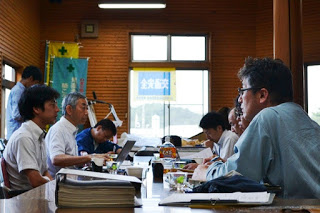 会議室のような場所でテーブルを囲んで数人が座り話し合っている様子を写した写真