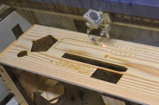 レーザー加工機で木の板に定規や絵馬の形を彫刻している作業中の様子の写真