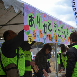 テントに「ありがとうございます」の文字が書かれ、スタッフの人が集まっている様子を写した写真