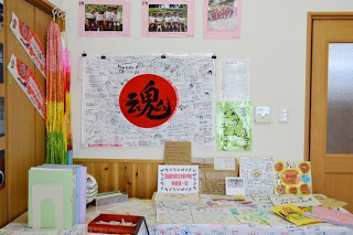 壁に被災地の写真や寄せ書き、折り鶴が飾られていて、正面に「魂」と書かれた大きな円形のポスターがある展示コーナーの展示の様子の写真