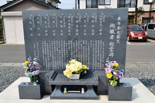 「東日本大震災 殉職者慰霊碑」の文字と、10名の名前が刻まれた黒い石碑の前に色とりどりの花が丁寧に供えられている写真