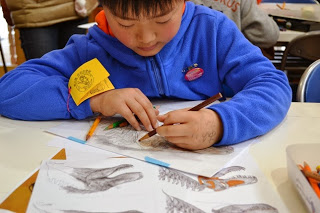 男の子が机の上の恐竜のイラストを色鉛筆で熱心に塗っている様子の写真