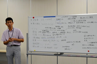 たくさんの意見で埋め尽くされたホワイトボードの横に講師の男性が立っている写真