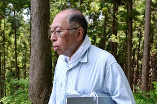 首元にタオルを巻いた佐藤さんが森林の中を歩いている様子を横から写した写真