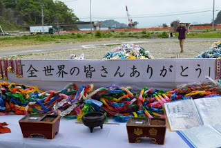 「全世界の皆さんありがとう」と書かれた横断幕の下に、カラフルな千羽鶴や香炉、募金箱などが並べられた祭壇のようすの写真