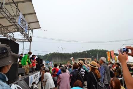 ステージから出演者たちが餅を客席に向かって投げ、たくさんの観客が手を伸ばして受け取ろうとしている賑やかな様子の写真