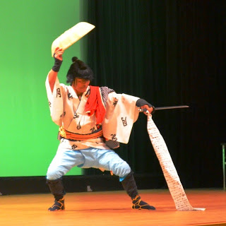 男性が着流し姿で右手で笠を持ち左手を前に出しながら踊っている写真