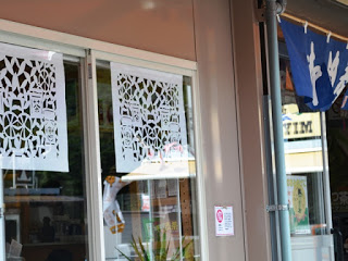 店舗のガラス窓に、白い切り絵作品が飾られている写真