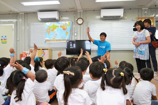 前方に座る長谷部選手が右手を上げ、目の前の園児たちも同じように手を挙げている室内の写真