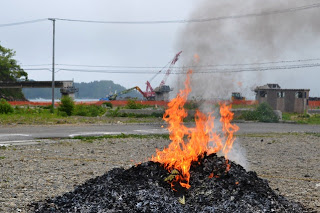 地面の上で黒くなった千羽鶴の山が炎と煙を上げて燃やされている様子を近くから捉えた千羽鶴の供養焼却の写真