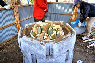 コンクリートブロックで囲まれた円形の炉の中に切りそろえた竹材がぎっしり詰められている様子を上から写した、炭の原料をセットした直後の写真