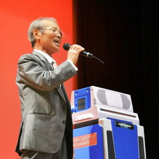 スーツ姿の男性がマイクを片手に歌を歌っている写真