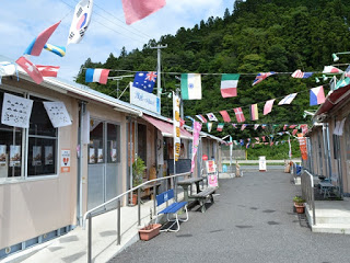 万国旗が飾られた仮設商店街の店舗前に切り絵の作品が飾られている様子が見える写真