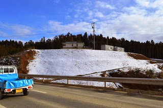 道路の奥の高台の斜面に雪が積もっている様子を写した写真