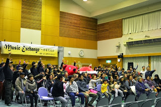 音楽イベントの最後に参加者全員が客席に並び、笑顔で手を上げながら盛り上がっている様子の写真