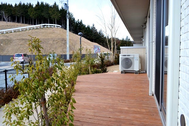 駐車場が奥に見えエアコンの室外機が置かれたウッドデッキを写した写真