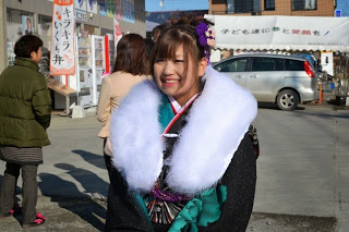 会場の屋外で、黒と緑色の振袖と白いファーを身につけた笑顔の女性をアップで撮影した写真