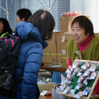 青いジャンバー姿の女性が商品をテーブルに置いて目の前のスタッフの人と会話している写真