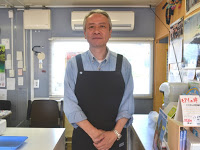 エプロン姿の阿部さんが手を前に組んで正面をみている写真