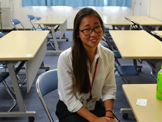 パイプ椅子に座って笑顔の亀山さんの写真