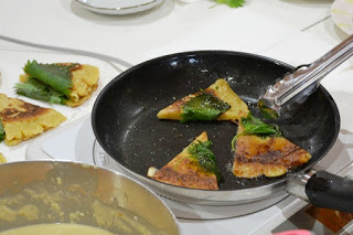 紫蘇がのせられた三角形の食べ物をフライパンで調理している写真