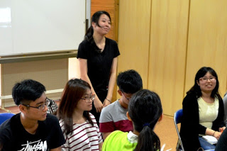 前列に座っている学生たちの中で、黒い服の女性が立ち上がって自己紹介をしている写真