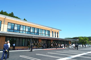 人々が出入りする様子が見える、新しく建てられたベージュ色の外壁の二階建ての施設を斜め正面から広く撮影した写真