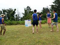 青いビブスを着た5人の男性が芝生の上に立っている様子の写真