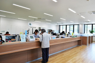 明るい木目の床と広いカウンターのある窓口で、男性が職員の女性と対面して手続きをしている写真