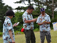 同じ水色のアロハシャツを着た男性3名がメモのようなものをみている写真