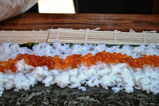 巻きすの上に海苔と白いご飯、中央にイクラが並べられている巻き寿司をアップで撮影した写真