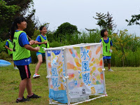 緑のビブスを着た子供たちが「水風戦」と書かれた看板の後ろで構えている試合中の様子の写真