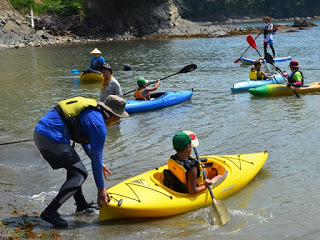 浅瀬でライフジャケットを着た参加者たちがカヤックに乗り、水面をゆっくりと進みながら水掻きの実践練習を行っている写真