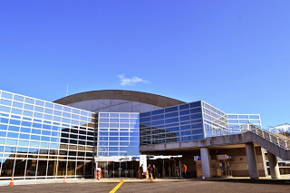 青空の下、入り口には晴れ着姿の新成人が数人立っている、ガラス張りの近代的な大きなベイサイドアリーナの建物外観の写真