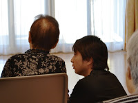 椅子に座っている施設利用者の女性の横に男性がしゃがみ込んでしゃべりかけている写真