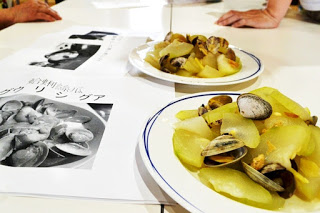 料理のレシピや説明の紙が置かれ、傍に白い皿に盛られた、アサリと大根のような具材が盛り付けられた料理が2皿並んでいる写真