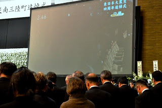 大勢の人々がスクリーンの前に集まっている様子を写した写真