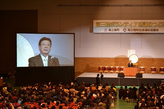 大きなモニターに佐藤市長の顔が映し出されている会場内の写真