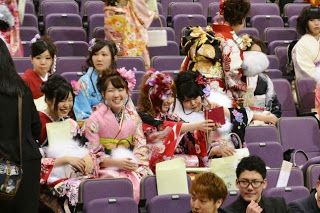 会場の座席に色とりどりの振袖を着た女性たちが座って談笑したり、スマートフォンで自撮りをしている写真