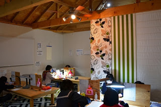 屋内の照明の下、木の机に向かって数人の子どもたちが勉強に集中しており、落ち着いた雰囲気の中で学習支援が行われている様子の写真