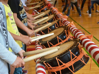 体育館の中で子どもたちが小太鼓の前に横一列に並び、両手で持ったバチを太鼓の上に置いている写真