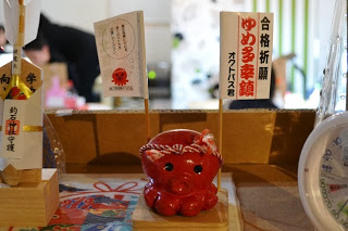 合格祈願と書かれた旗を背負った赤いタコの置き物「オクトパス君」が台の上に飾られ、横にはお守りも飾られている様子を写した写真