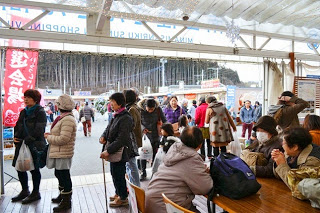 屋根付きの飲食スペース内から外を見た構図になっており、テーブル席でくつろぐ人々と、外を歩く来訪者が同時に写っている様子を写した写真