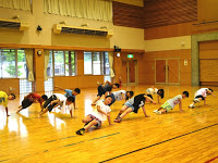 体育館の広い床の上で、複数の子供たちが手をついて体を支えながら運動している様子の写真