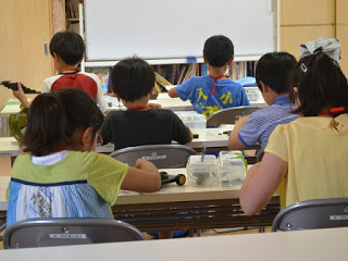 教室内で長机に2名ずつそれぞれの机に座り、ロボット作成をしている様子を後方から写した写真