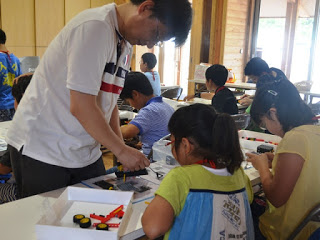 講師の猪狩憲一さんが長机に置かれたロボットのパーツについて女の子に説明をしている写真