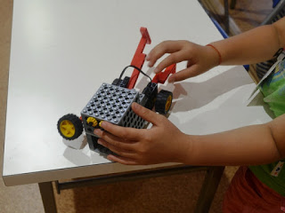 グレーの四角い車体に車輪がつき、前面に赤いアームのような部品が立っている自走ロボット「ペッパーくん」を子どもが両手で操作している写真